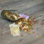 A glass jar with euro coins and banknotes spilled on a wooden surface, representing finance and savings.