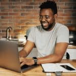 African American man smiling while working remotely on laptop from home office