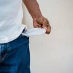 A person in jeans reveals an empty pocket, symbolizing financial hardship.